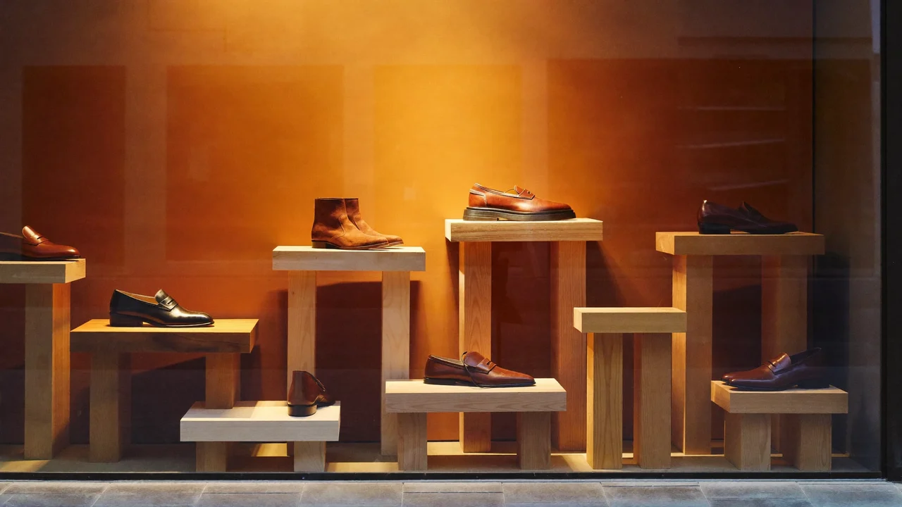 Vetrina illustrata al crepuscolo con poche scarpe su semplici rialzi in legno.